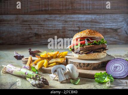 Hamburger mit Kichererbsen-Patty, Tomaten, Pilzen und Gemüse auf Roggenbrot. Um, Pommes, Pilze und Spargel. Speicherplatz kopieren. Horizontale Aufnahme. Stockfoto