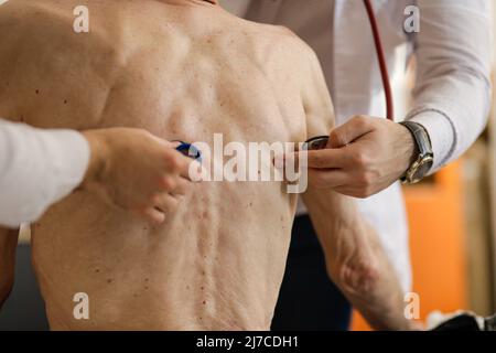 Ein Sanitäter und ein Sanitäter überprüfen die Gesundheit eines älteren männlichen Patienten mit Stethoskop. Stockfoto