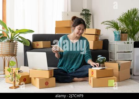 Asiatische Frau Unternehmerin mit Rechner mit Bleistift in der Hand, Berechnung der finanziellen Kosten zu Hause Büro, Online-Markt Verpackung Box Lieferung Stockfoto