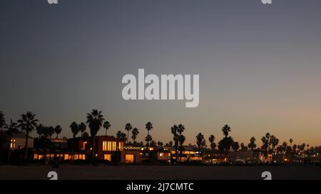 Palmen Silhouetten in der Dämmerung Himmel, California Beach, USA. Palmen am Strand an der Sommerküste, pazifikküste in der Dämmerung. Fenster von Häusern oder Häusern am Abend. Architektur mit dunklem Kontrast. Stockfoto