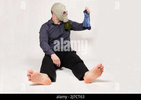 Ein barfuß Mann in einer Gasmaske hält schmutzige stinkende Socken. Das Problem des unangenehmen Fußgeruchs bei Männern Stockfoto