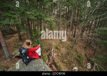 Frau, die auf einem Felsblock mit Nordic-Walking-Stöcken sitzt Stockfoto