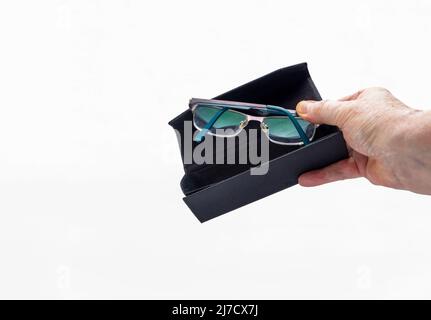 Mann, der seine Glasbrille in einem zusammenklappbaren schwarzen Gehäuse vor einem weißen Hintergrund ablegt Stockfoto