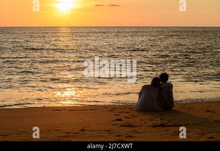 Ein Paar sitzt am Strand und beobachtet den Sonnenuntergang in Khao Lak, Phang Nga. Beliebtes Touristenziel im Süden Thailands Stockfoto