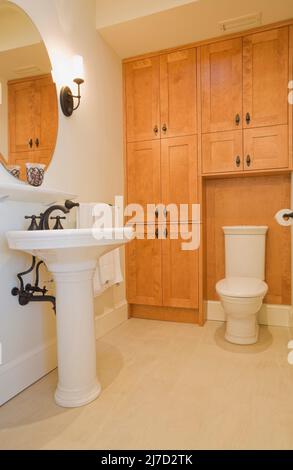 Weißes Standwaschbecken und Toilette mit hohem Tank im Gästebad im luxuriösen Zuhause. Stockfoto