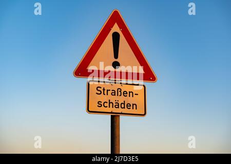 Straßenschild mit Warnung vor Straßenschäden. In deutscher Sprache heißt es "Straßenschäden", was den Verkehr aufgrund einer holprigen Straße verlangsamen sollte. Stockfoto