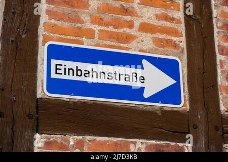 Einbahnstraße Verkehrsschild an einer Hauswand in deutscher Sprache. Straßenschild eines weißen Pfeils auf einer blauen Metallplatte. Einbahnstraße in schwarzen Buchstaben. Stockfoto