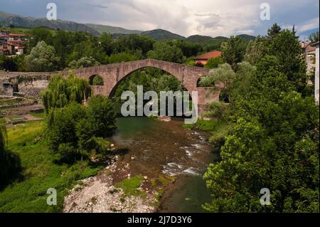 Über dem Fluss Ter und dem anmutigen Pont Vell oder der Alten Brücke in Sant Joan de les Abadesses, Ripollès, Katalonien, Spanien. Die ursprüngliche romanische Brücke, die in den 1100er Jahren n. Chr. erbaut wurde, wurde in den 1400er Jahren im gotischen Stil mit einem schlanken Hauptbogen rekonstruiert, der als der leichteste seiner Art auf der Iberischen Halbinsel gilt. Stockfoto