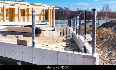 Betonfundament mit Entwässerungslöchern des Zauns für ein modernes Holzhaus aus verleimtem Schichtholz. Bau eines Hauses am Ufer von Stockfoto