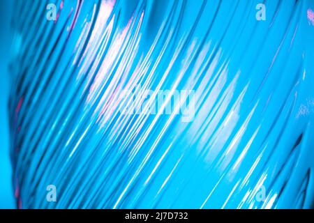 Abstrakter Glashintergrund. Textur aus gewelltem Glas, beleuchtet mit mehrfarbigem Licht. Rosa und blaue Flecken. Nahaufnahme. Fackeln auf Glas. Stockfoto