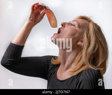 Eine blonde Frau hält ein Stück Parmaschinken, Italien, in ihrer Hand neben ihrem Mund, als sie es essen will Stockfoto