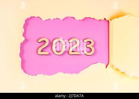Holznummern 2023 Silhouette mit grob zerrissenem rosa Papierloch auf hellem Hintergrund. Neujahrsbeginn Glückwünsche und Planungskonzept. Stockfoto