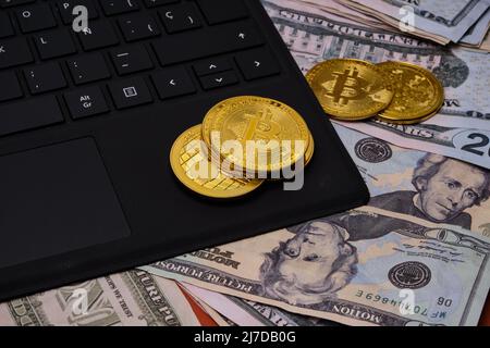 Nahaufnahme eines Laptops mit einigen Bitcoins auf einem Dollarhaufen. Stockfoto