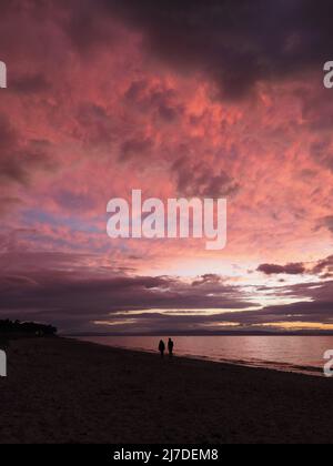 Rosa und rote Farben eines feurigen Sonnenuntergangs nach dem Nachglühen auf den Wolken über dem Nairn Central Beach. Die Silhouetten eines Paares, das im Vordergrund läuft. Stockfoto