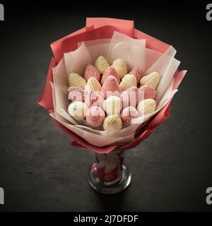 In einer Vase auf schwarzem Hintergrund steht ein Bouquet aus reifen Erdbeeren, bedeckt mit weißer und rosafarbener Schokolade Stockfoto