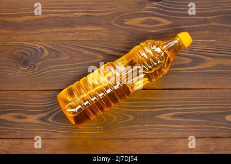 Öl in einer Flasche auf dem Tisch. Olivenöl in einer Plastikflasche mit gelbem Verschluss liegt auf braunen Holzbrettern. Eine Flasche Sonnenblumenöl in der Sonne. Schließen Stockfoto