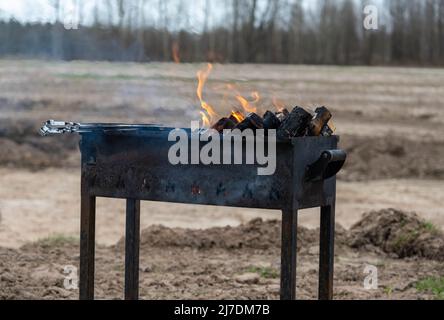 Brennende Holzstämme mit einer orangen Flamme auf einem offenen Grill im Freien. Stockfoto