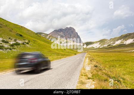 Ein Auto auf einer Bergstraße. Touristen auf einer Straße des Apennins in den Abruzzen, Italien. Das Campo Imperatore-Hochplateau mit dem Gran Sasso Stockfoto