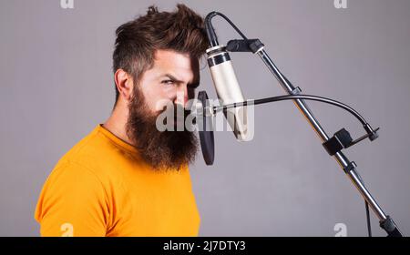 Männlicher Profisänger im Studio. Musikproduktion. Bärtiger Mann singt im Kondensatormikrofon. Stockfoto