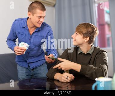 Vater gibt seinem Teenager-Sohn Taschengeld. Sohn, danke Vater Stockfoto