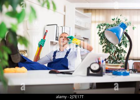 Mann in Uniform spricht am Telefon, anstatt Büro zu putzen Stockfoto