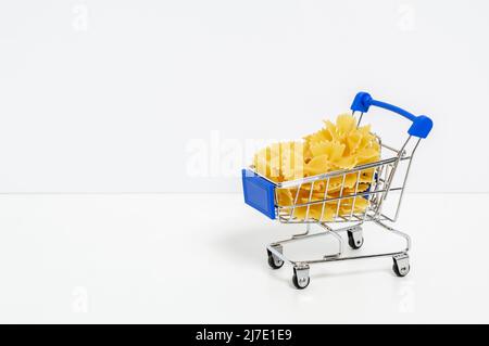 Farfalle Pasta in blauem Einkaufswagen isoliert auf weißem Hintergrund mit Texthintergrund. Lebensmittel- und Lebensmitteleinkäufe, Preiserhöhung, Lebensmittelkrise Stockfoto