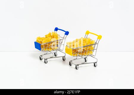 Ungekochte Farfalle Pasta in blauen und gelben Einkaufswagen in den Farben der ukrainischen Flagge isoliert auf weißem Hintergrund. Nahrungsmittelkrise, Preiserhöhung Stockfoto