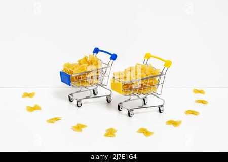 Ungekochte Farfalle Pasta in blauen und gelben Einkaufswagen in den Farben der ukrainischen Flagge isoliert auf weißem Hintergrund. Nahrungsmittelkrise, Preiserhöhung Stockfoto