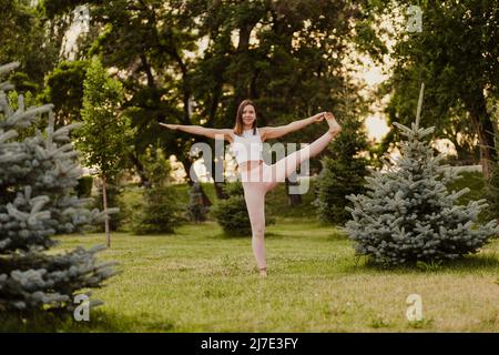 Junge sportliche Frau praktiziert Yoga. Schöne junge Frau praktiziert utthita hasta padangusthasana Yoga asana in der Natur Stockfoto