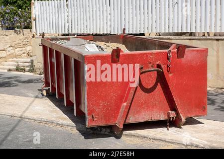 Bauabfälle in einem halbleeren roten Müllcontainer. Behälter aus Metall, gefüllt mit Bauabfällen, Schutt in der Nähe einer Baustelle. Stockfoto