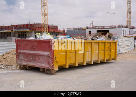 Bauabfälle in einem riesigen überlasteten Müllcontainer. Behälter aus Metall, gefüllt mit Bauabfällen, Schutt in der Nähe einer Baustelle. Stockfoto