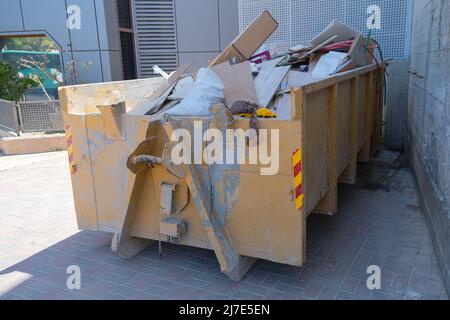 Bauabfälle in einem riesigen überlasteten Müllcontainer. Behälter aus Metall, gefüllt mit Bauabfällen, Schutt in der Nähe einer Baustelle. Stockfoto