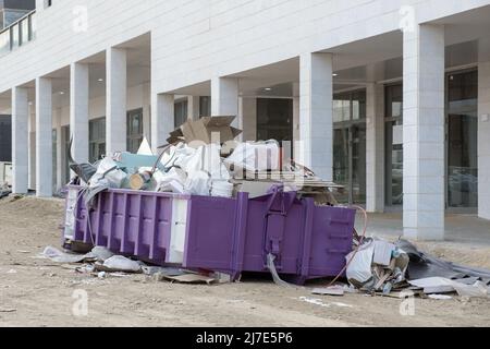 Bauabfälle in einem riesigen überlasteten Müllcontainer. Behälter aus Metall, gefüllt mit Bauabfällen, Schutt in der Nähe einer Baustelle. Stockfoto