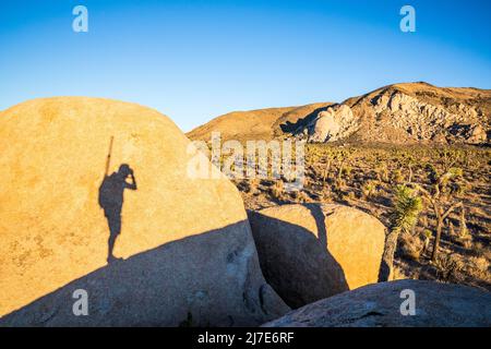 Der Schatten eines Mannes, der auf einen Felsbrocken gegossen wurde, während er im Joshua Tree National Park ein Foto macht. Stockfoto