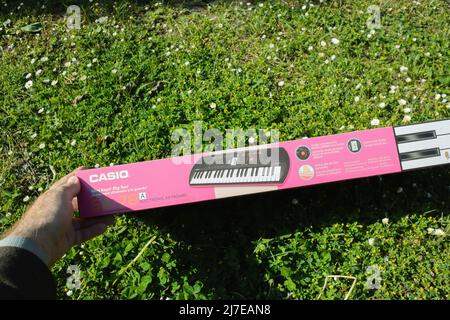 Dortmund, Deutschland - Mai 8 2022: POV männliche Hand hält neue Casio SA-78 Mini-Keyboard Klavier in grünen Garten Gras Blick auf die Seitenspezifikationen Stockfoto