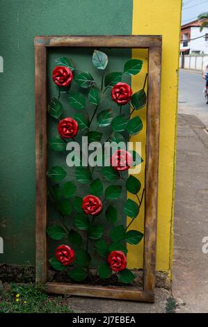 Rote Metallblumen in einem Holzrahmen, der außerhalb des Rosa de Saron-Geschäfts zum Verkauf angeboten wird und auf Gegenstände der Metallhandwerkskunst spezialisiert ist. Stockfoto