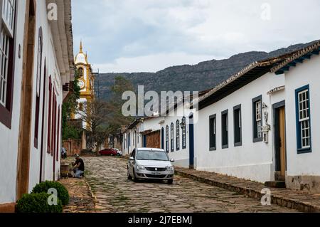 Blick auf die bergauf gelegene Padre Toledo Straße mit Kolonialhäusern auf beiden Seiten inmitten des historischen Zentrums von Tiradentes und unter wolkenbedecktem Himmel. Stockfoto