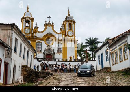 Die berühmte Santo Antonio Mutterkirche, umgeben von Kolonialhäusern, in der Rua da Camara Straße im historischen Zentrum von Tiradentes unter bewölkten Himmel. Stockfoto