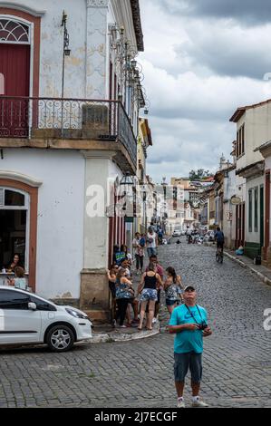 Blick auf die Getulio Vargas Straße mit vielen Fußgängern, die mitten im historischen Zentrum von Sao Joao del Rei unter wolkenverdecktem Himmel herumlaufen. Stockfoto