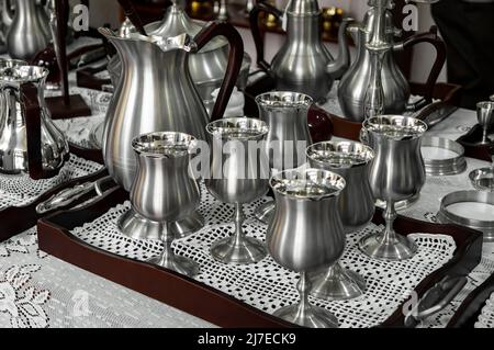 Einige Zinnkelche und ein Glas auf einer Tischplatte zum Verkauf im FAEMAM-Geschäft im historischen Zentrum von Sao Joao Del Rei. Stockfoto