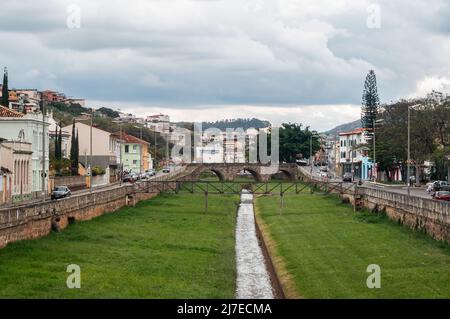 Südwestlicher Blick auf viele koloniale Gebäude in der Innenstadt mit einem schmalen Wasserkanal in der Mitte, umgeben von Grasfeldern. Säge von der Cadeia-Brücke. Stockfoto