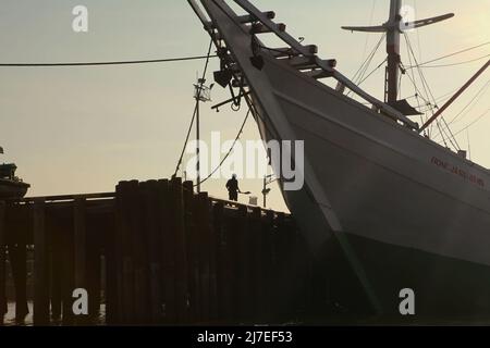 Ein traditionelles Phinisi-Schiff und die Silhouette eines Arbeiters, der auf einem Pier steht; fotografiert vom Fluss Musi in Palembang, Süd-Sumatra, Indonesien. Stockfoto