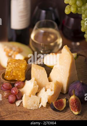Käseplatte serviert mit Trauben, Melone, Feigen, Cracker, Honig, Nüsse und Weißwein auf einem Holztisch Stockfoto