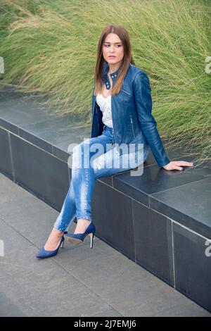 Frau in blauer Lederjacke sitzt im Freien und schaut weg Stockfoto