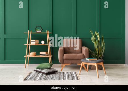 Stilvolles Interieur des Zimmers mit Sessel und Regal in der Nähe der Farbwand Stockfoto