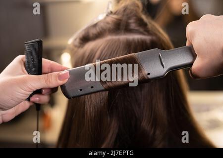 Nahaufnahme der Hände des Meisters im Spa-Salon Glätten Sie die Haare mit einem Bügeleisen im Spa-Salon. Stockfoto