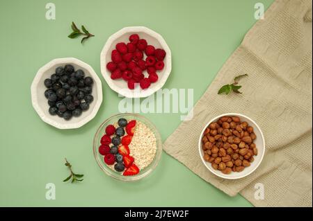 Flache Lage von Beerenfrüchten und Minzblättern auf pastellgrünem Hintergrund Stockfoto