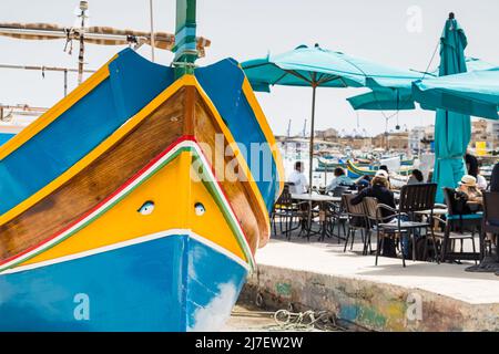 Luzzu Boot gesehen auf der Promenade in Marsaxlokk neben einem Restaurant im April 2022. Stockfoto