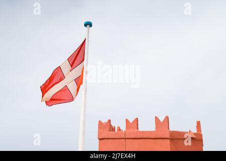 Die Flagge des Johannisordens weht im Wind auf dem Roten Turm (oder dem St. Agatha’s Tower), der im Mai 2022 über einem Hügel in Mellieha, Malta, gesehen wurde. Stockfoto