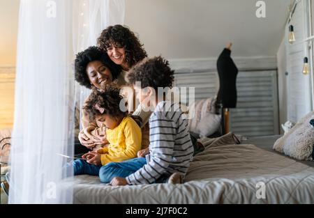 Glückliche multiethnische Familie. Lächelnde schwule Frauen verbringen zu Hause Zeit mit Kindern. Stockfoto